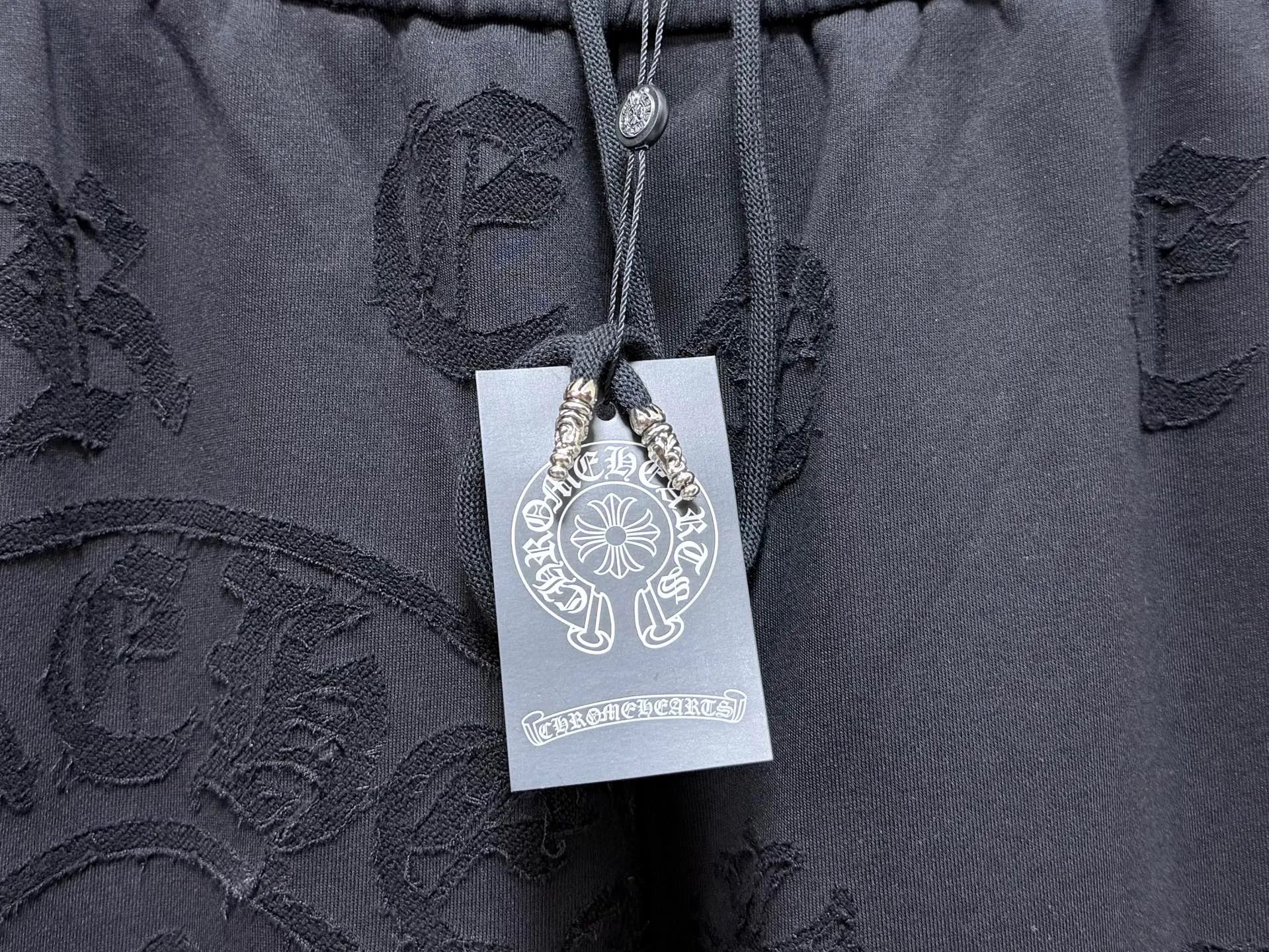 CH/Cro Heart 2026ss Burnt Flower Straight-leg Sweatpants Classic heavy-weight sweatpants with gray tones, Retro street style full-fitting, direct recognition, same style for men and women. ●Three-dimensional patchwork technology: The whole body is covered with Gothic letters + cross flower totems, using raw edge patchwork embroidery, with a mustache-like old texture, and uneven and layered patterns. It is not an ordinary print, and it is durable and not easy to fall off. ●Style tailoring: Loose, straight and wide-legged version, modifying the shape of the legs, hiding the flesh neatly, not flattering the figure, with an online drape, and the upper body has a relaxed street tone. ●Fabric and waist: Heavy knitted terry fabric, thick and soft, with good drape; elastic drawstring waist, with branded metal engraved rope ends, easy to put on and take off, and strong waist adaptability. ●Detailed design: The side pockets are convenient for carrying items, and the back pocket is decorated with cross-pattern patches. The front and rear patterns echo each other. Every detail is highly recognizable to the brand. ●Wearing scenarios: Suitable for street wear, daily outings, and trendy wear. Paired with sweaters, denim jackets, and leather jackets, you can easily create an American retro cool style. ●The overall gray base is paired with Cream White patches, which are low-key yet impactful. They are both comfortable and trendy. Versatile sweatpants, a must-have for fashionistas, are also available at the counter. SIZE：M L XL XXL XXXL